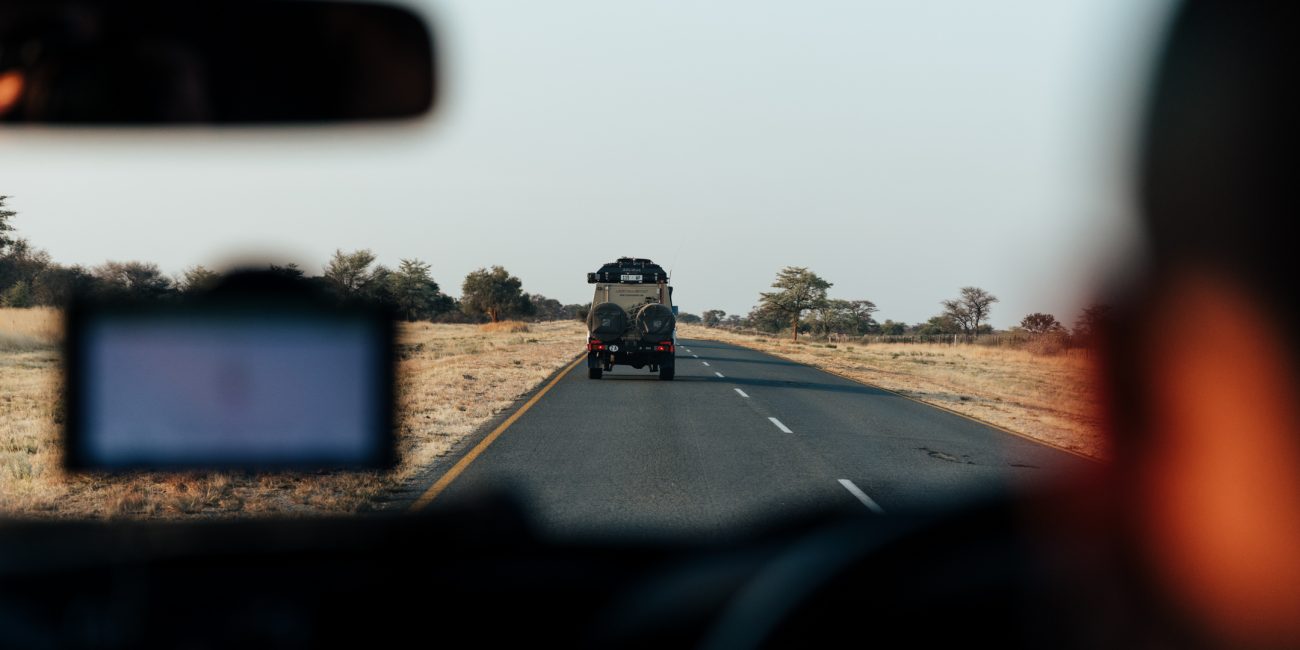 View from a vehicle's interior of a gravel road leading through the rugged terrain of Southern Africa, under a vast sky.