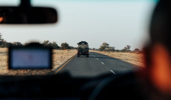 View from a vehicle's interior of a gravel road leading through the rugged terrain of Southern Africa, under a vast sky.