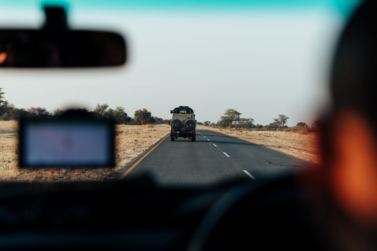 View from a vehicle's interior of a gravel road leading through the rugged terrain of Southern Africa, under a vast sky.